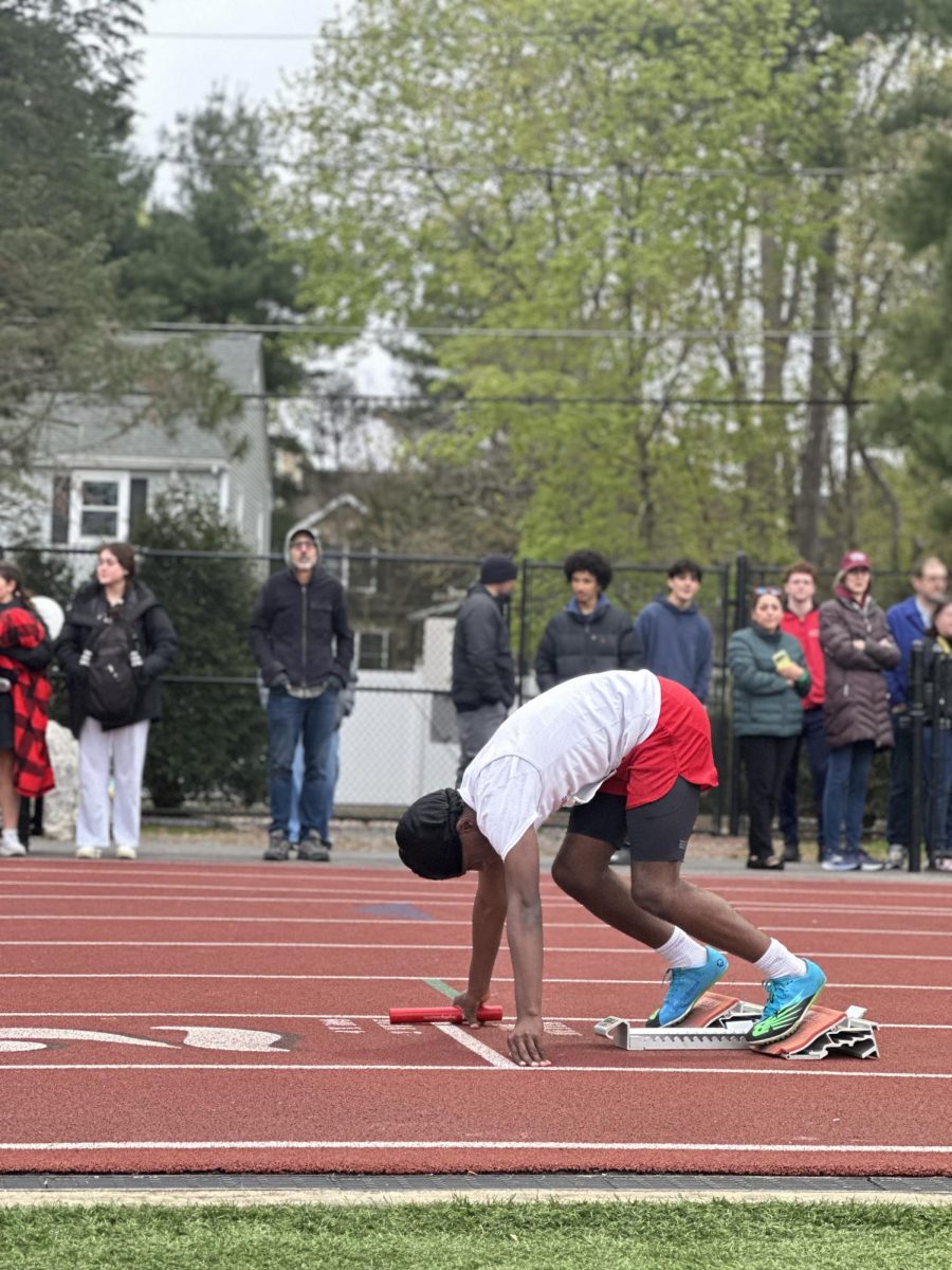 Junior Femi Okodjou crouches down on the starting blocks with the baton as the lead leg of the B team in the junior varsity 4x100-meter relay race. The A teams in both the varsity and JV races won the event, breaking 44.5 and 47 seconds, respectively.